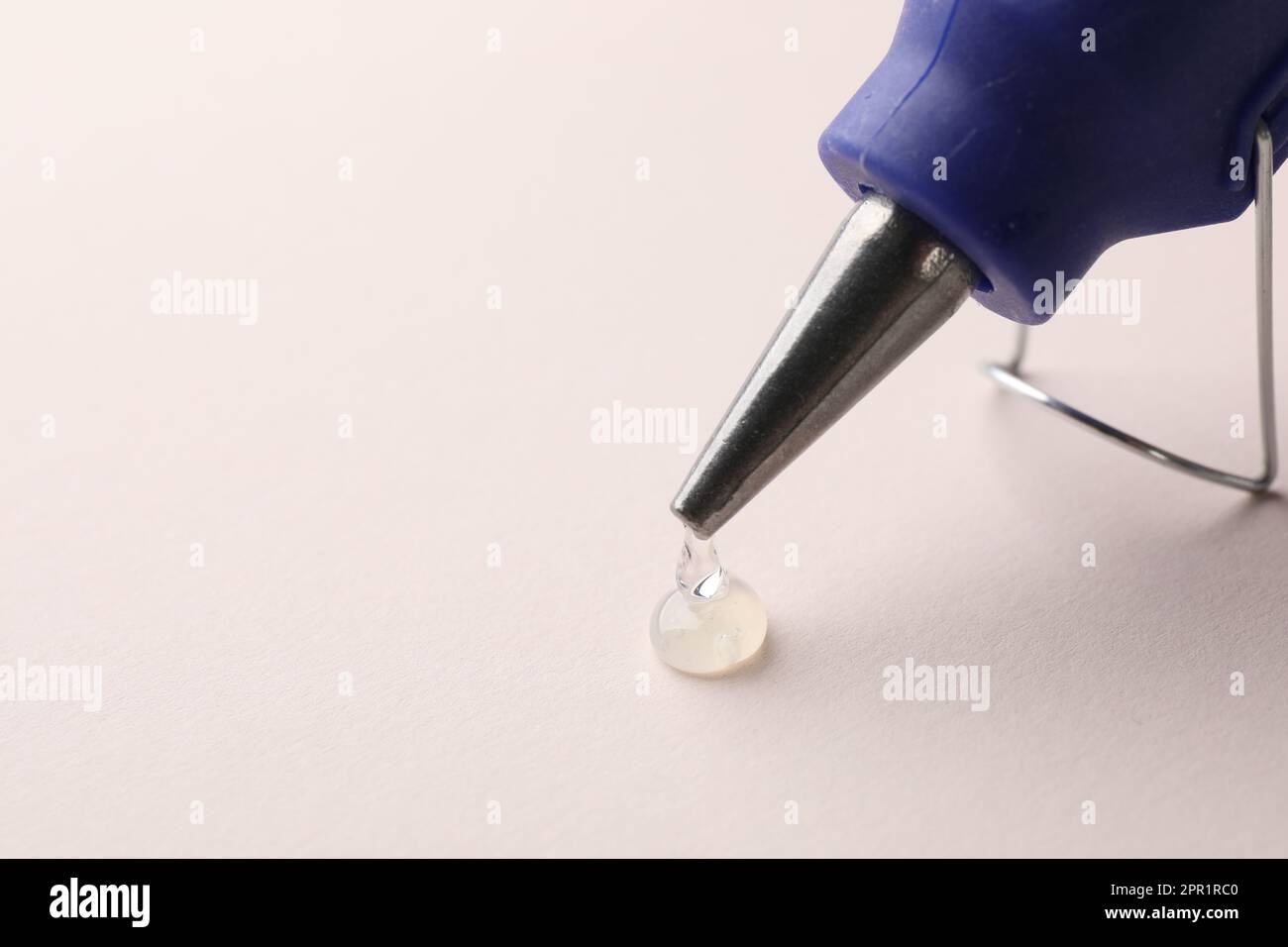Melted glue dripping from hot gun on white table, closeup. Space for