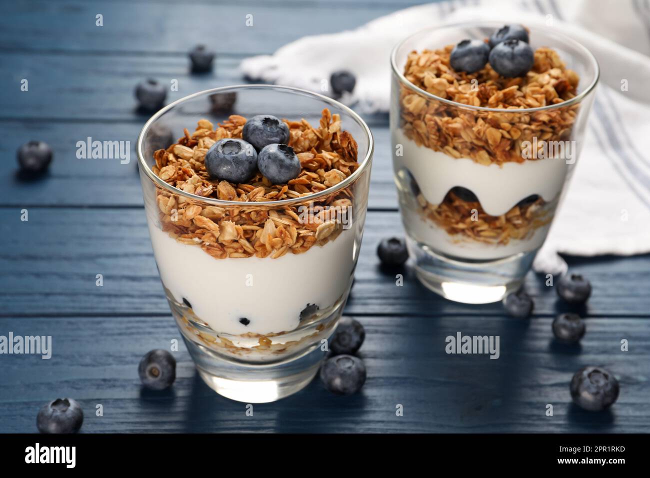 Glasses of tasty yogurt with muesli and blueberries on blue wooden table Stock Photo