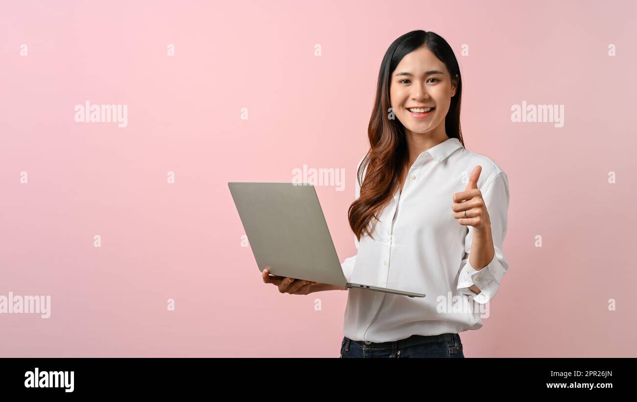 Image of young Asian woman holding laptop and give a thumbs up sign ...