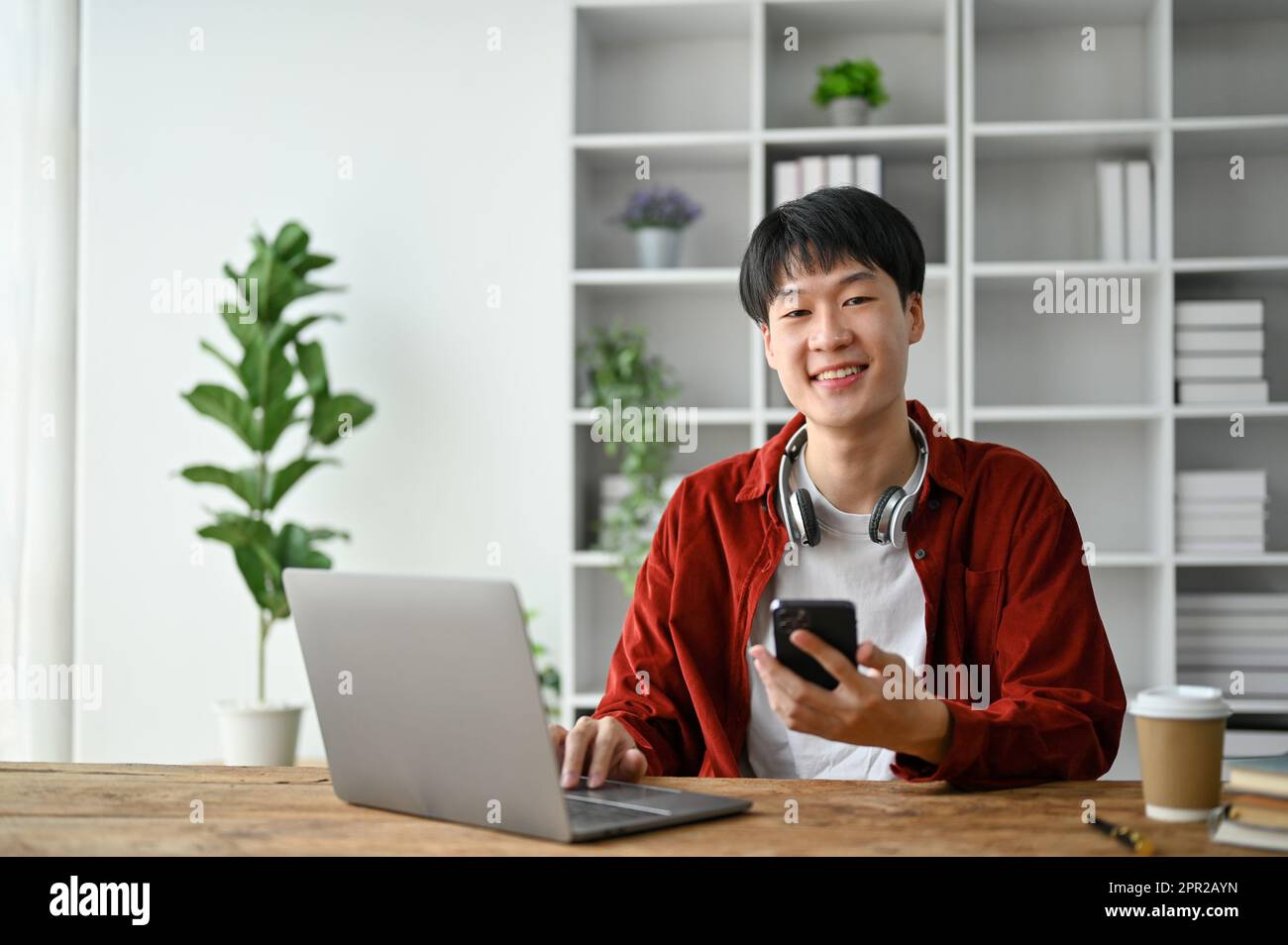 Cheerful young college student using laptop computer and smartphone while study in the study room. Stock Photo