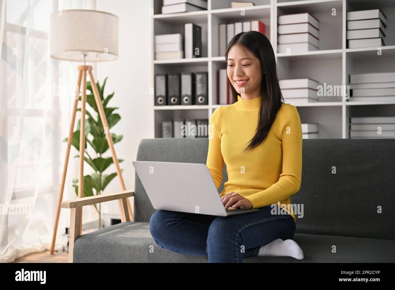 Young adorable Asian woman using laptop computer while sitting on the ...
