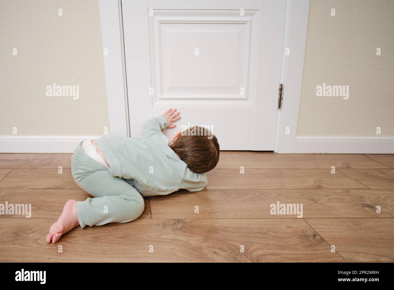 Little baby peeps under the door. Small child looks through the crack