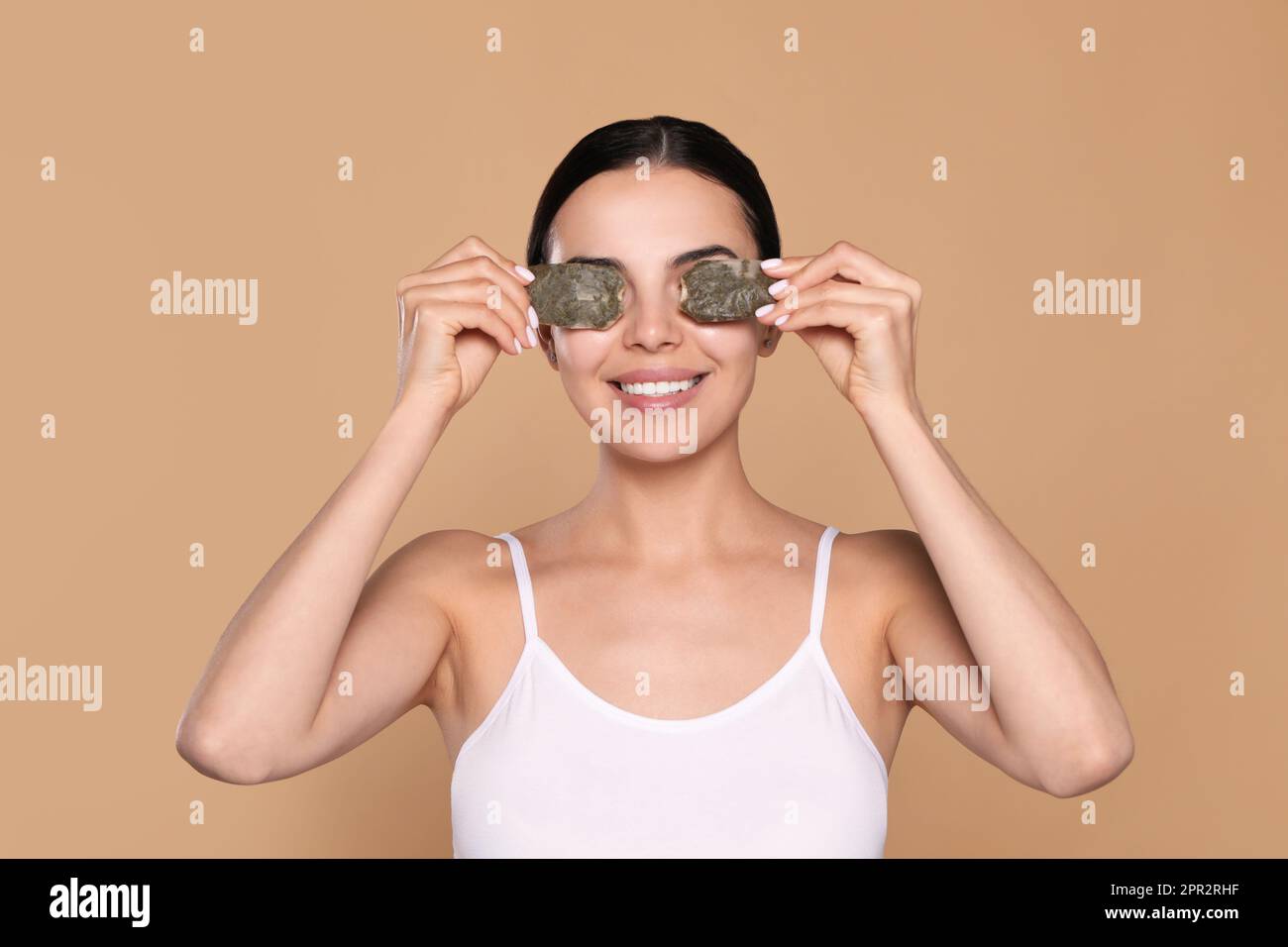 Beautiful young woman putting green tea bags on skin around eyes