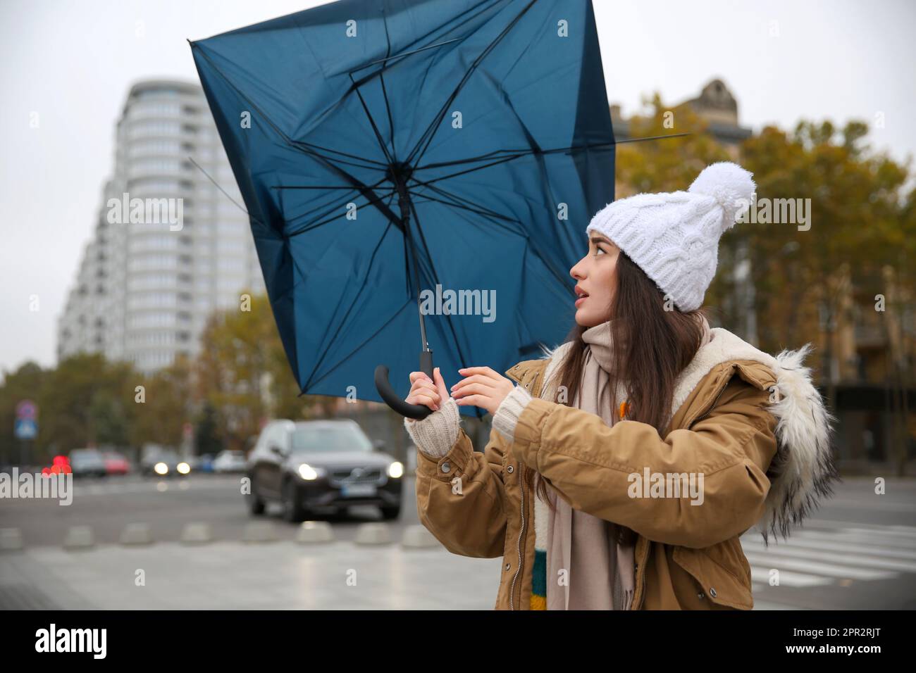 Woman with blue umbrella caught in gust of wind on street Stock Photo