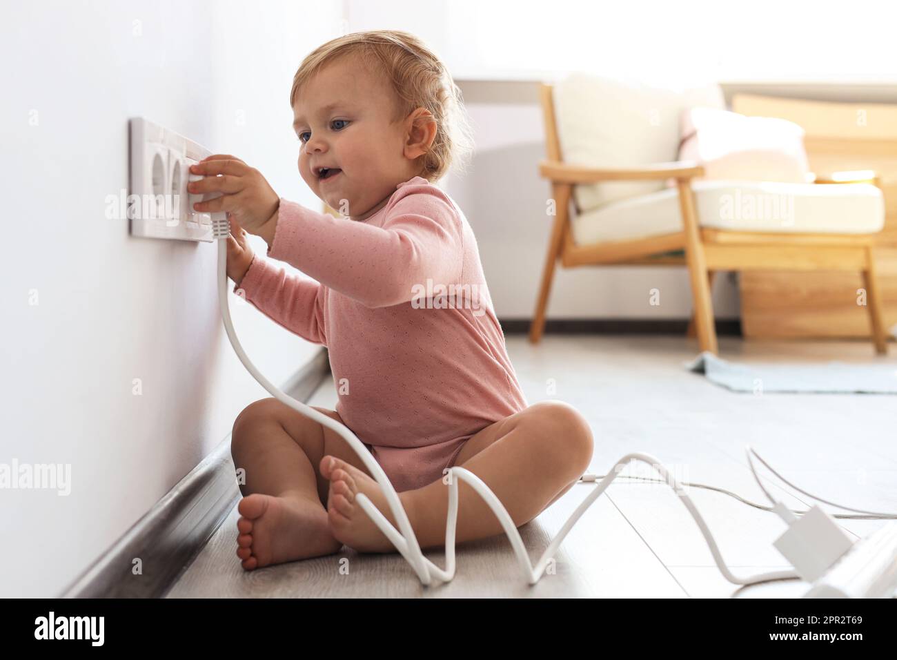 Cute baby playing with electrical socket and plug at home. Dangerous