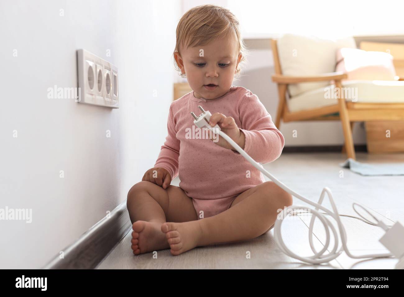 Cute baby playing with plug at home. Dangerous situation Stock Photo