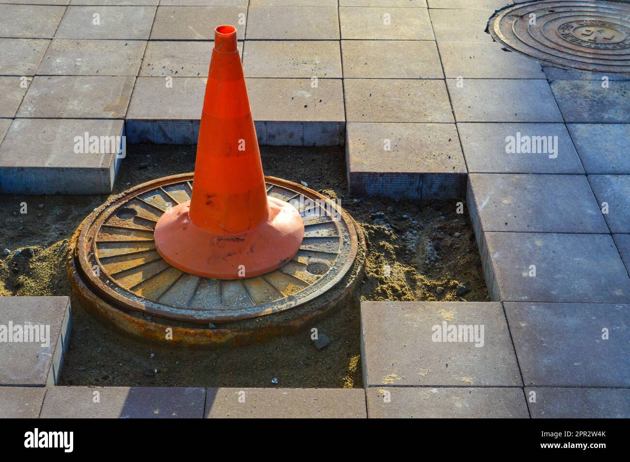 a bright orange cone stands on the sewer drain. marking of dangerous sections on the road, entry for people is prohibited. the cone stands on the brok Stock Photo