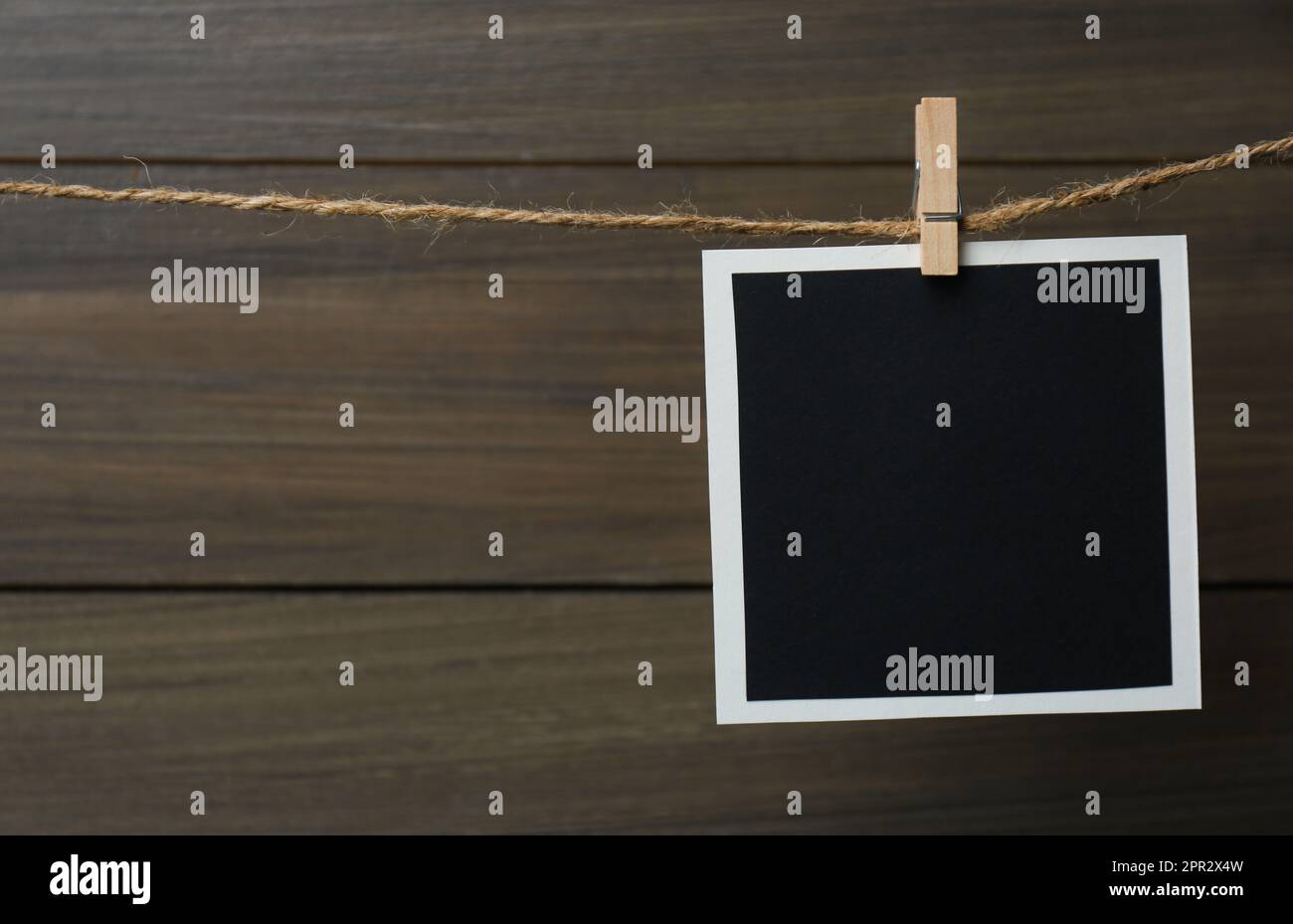 Clothespin with empty instant frame on twine against wooden background. Space for text Stock Photo
