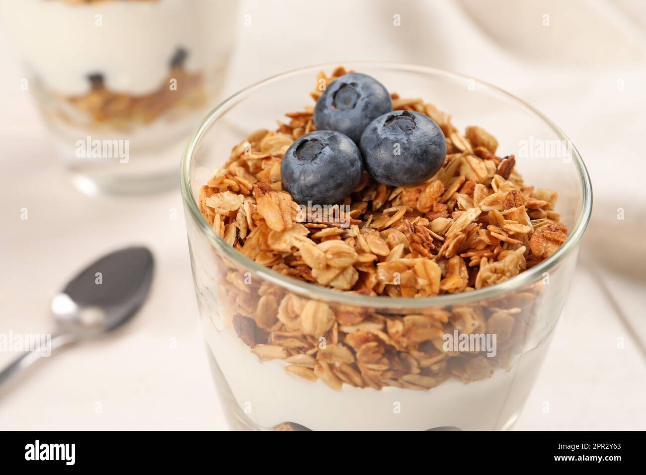 Glass of tasty yogurt with muesli and blueberries served on white table, closeup Stock Photo