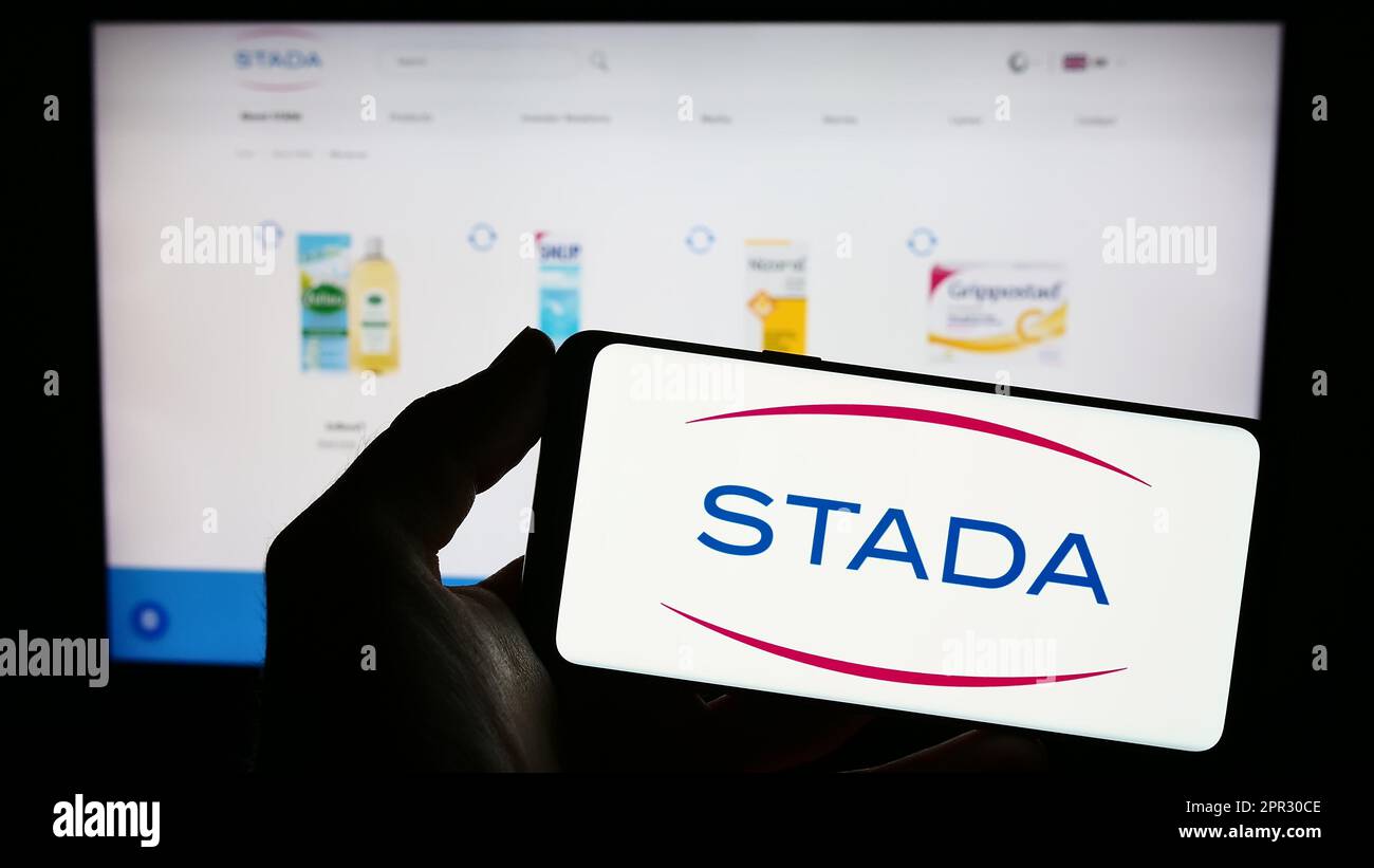 Person holding smartphone with logo of German company Stada Arzneimittel AG on screen in front of website. Focus on phone display. Stock Photo