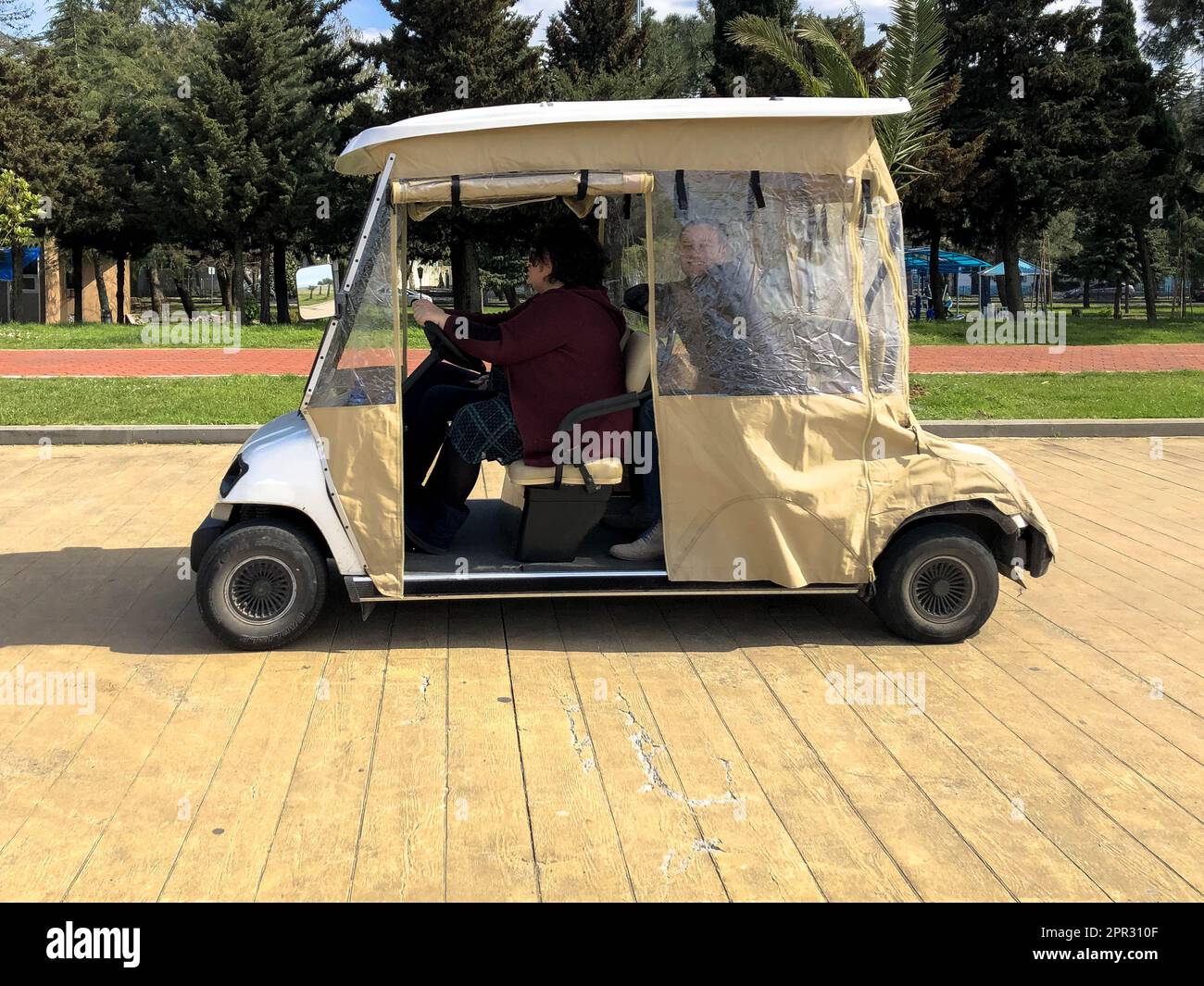 People ride in a small electric car, a golf car on the seafront on a sandy beach against the tropical green palm trees of the blue sky. Georgia, Batum Stock Photo