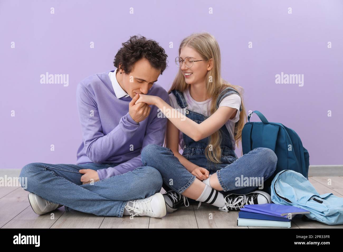 Teenage boy kissing his girlfriend's hand near lilac wall Stock Photo