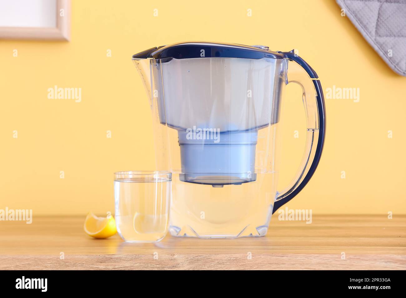 Modern filter jug, glass of water and lemon piece on kitchen counter