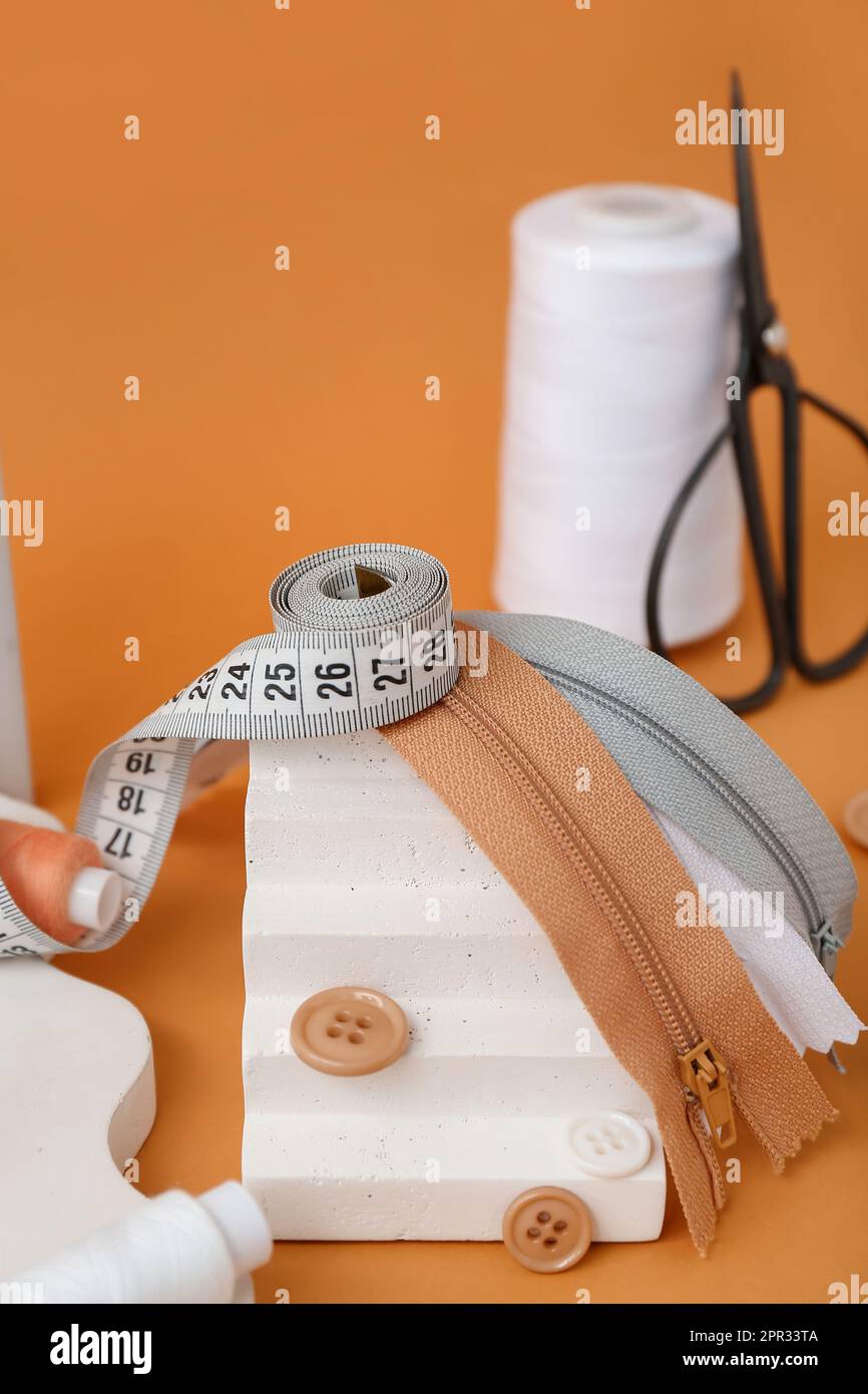 Podium with measuring tape, zips and buttons on orange background Stock