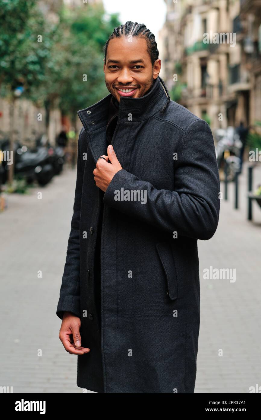 Confident and stylish African American man looking at camera and smiling while posing outdoors on the street. Stock Photo