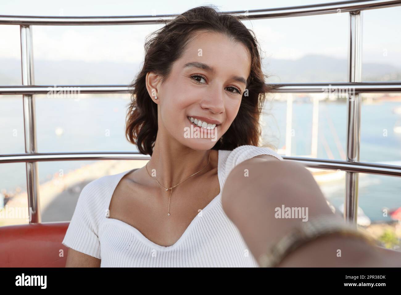 Happy young woman taking selfie on Ferris wheel near sea Stock Photo