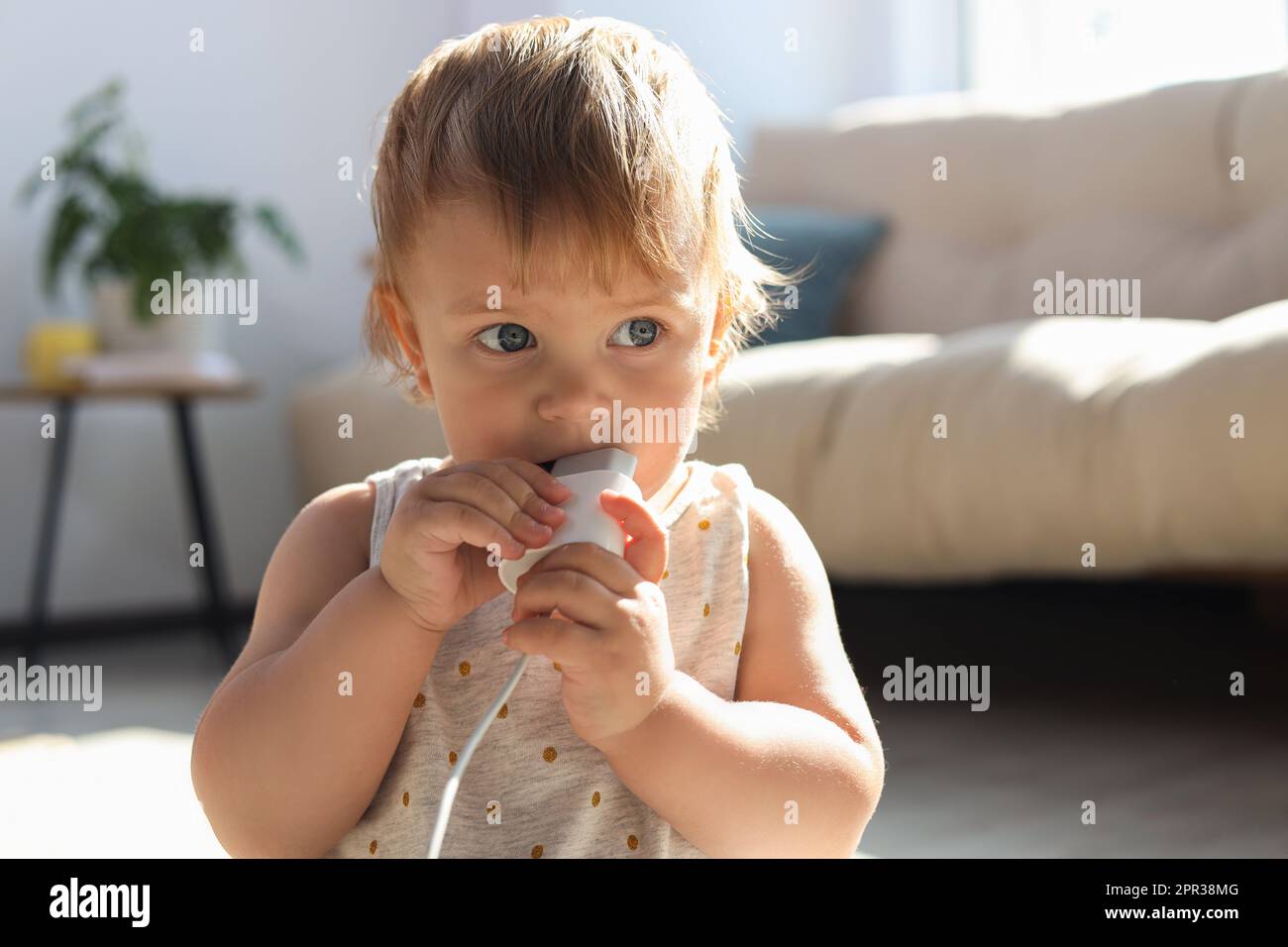 Cute baby with charger at home. Dangerous situation Stock Photo