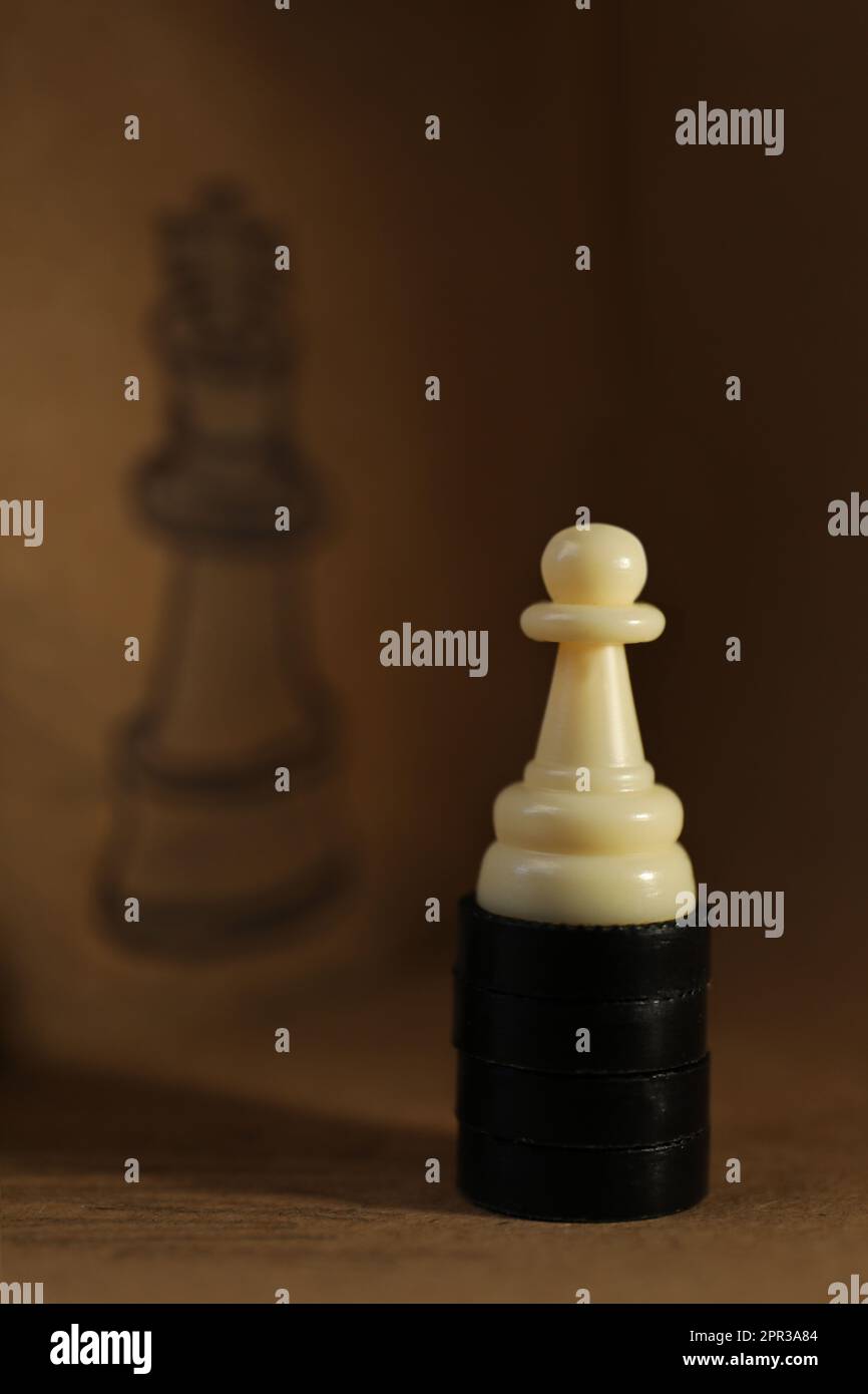 White pawn on wooden table in front of drawn queen chess piece Stock Photo