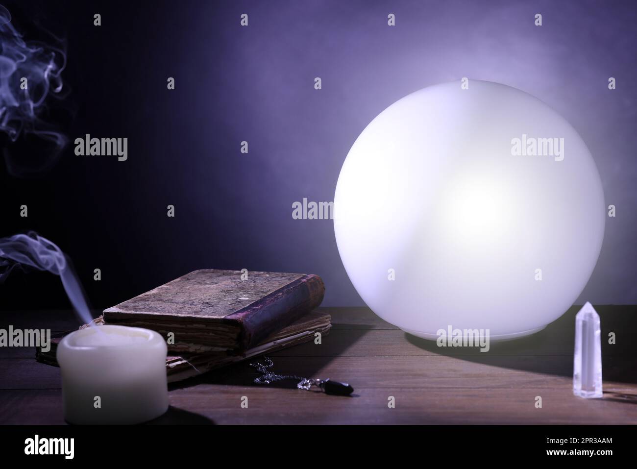 Prediction ball, books, stones and candle on table in darkness Stock Photo