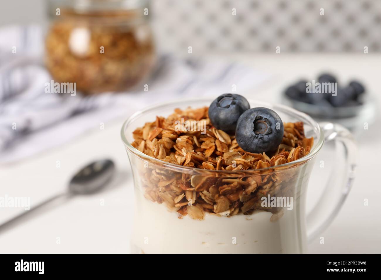 Tasty yogurt with muesli and blueberries in cup served on white table, closeup Stock Photo