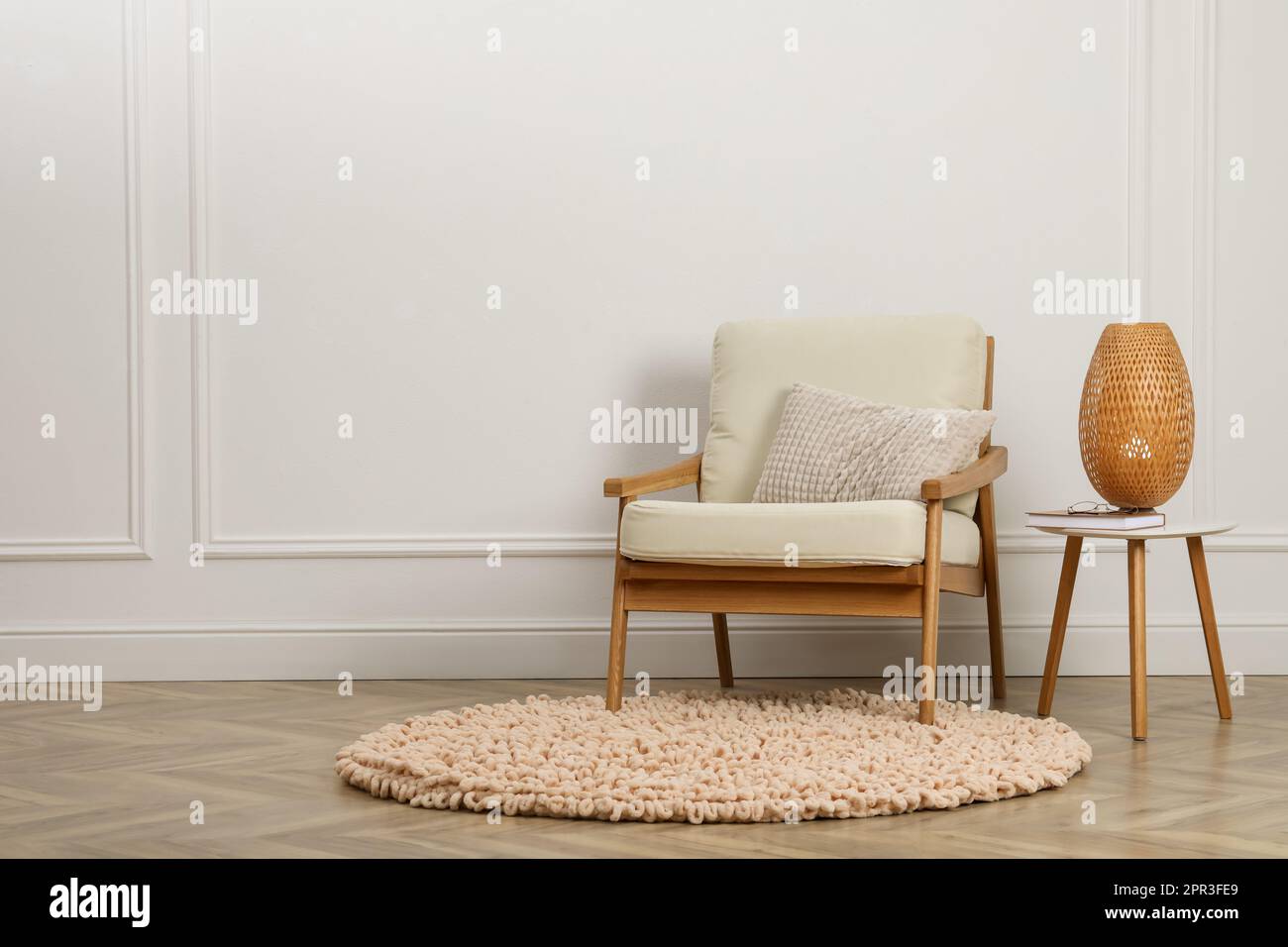 Stylish armchair with cushion and lamp near white wall indoors, space ...