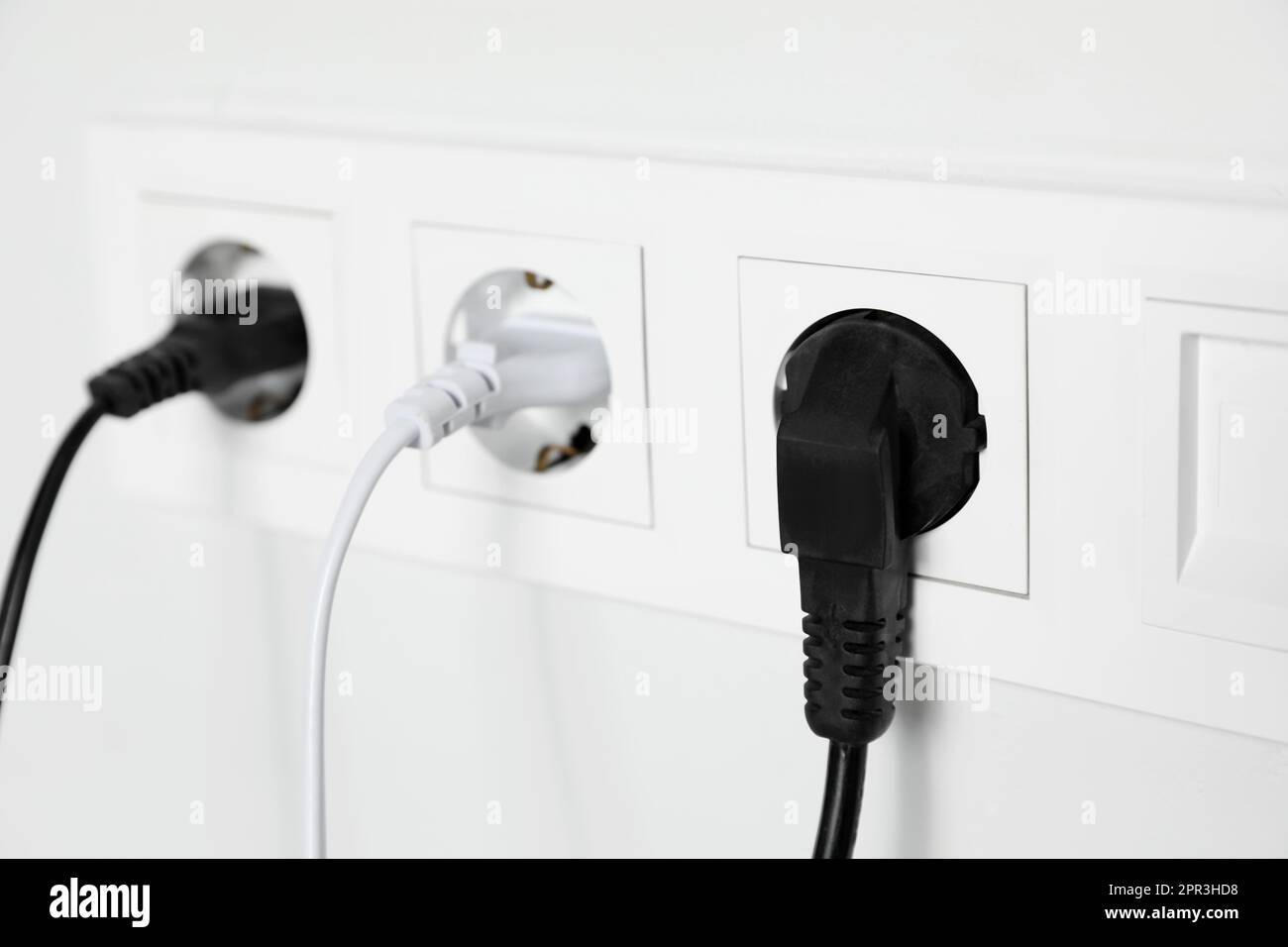 Power sockets with inserted plugs on white wall, closeup. Electrical