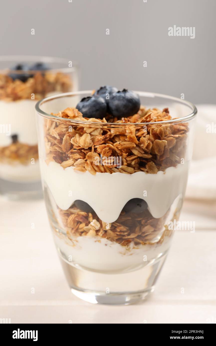 Glass of tasty yogurt with muesli and blueberries served on white wooden table Stock Photo