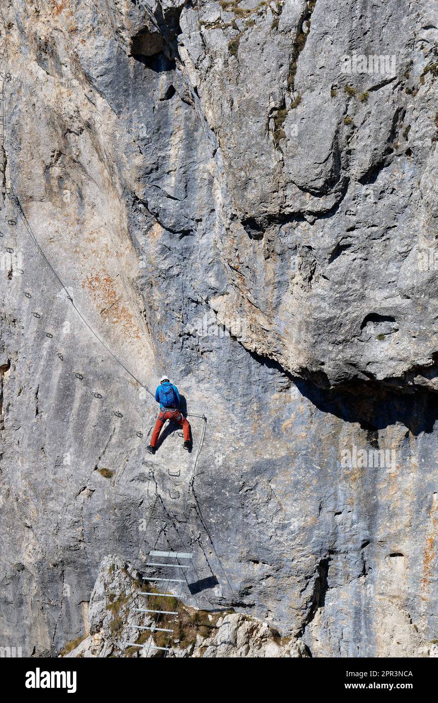 A person climbing a via ferrata route on a vertical rock wall. Sports