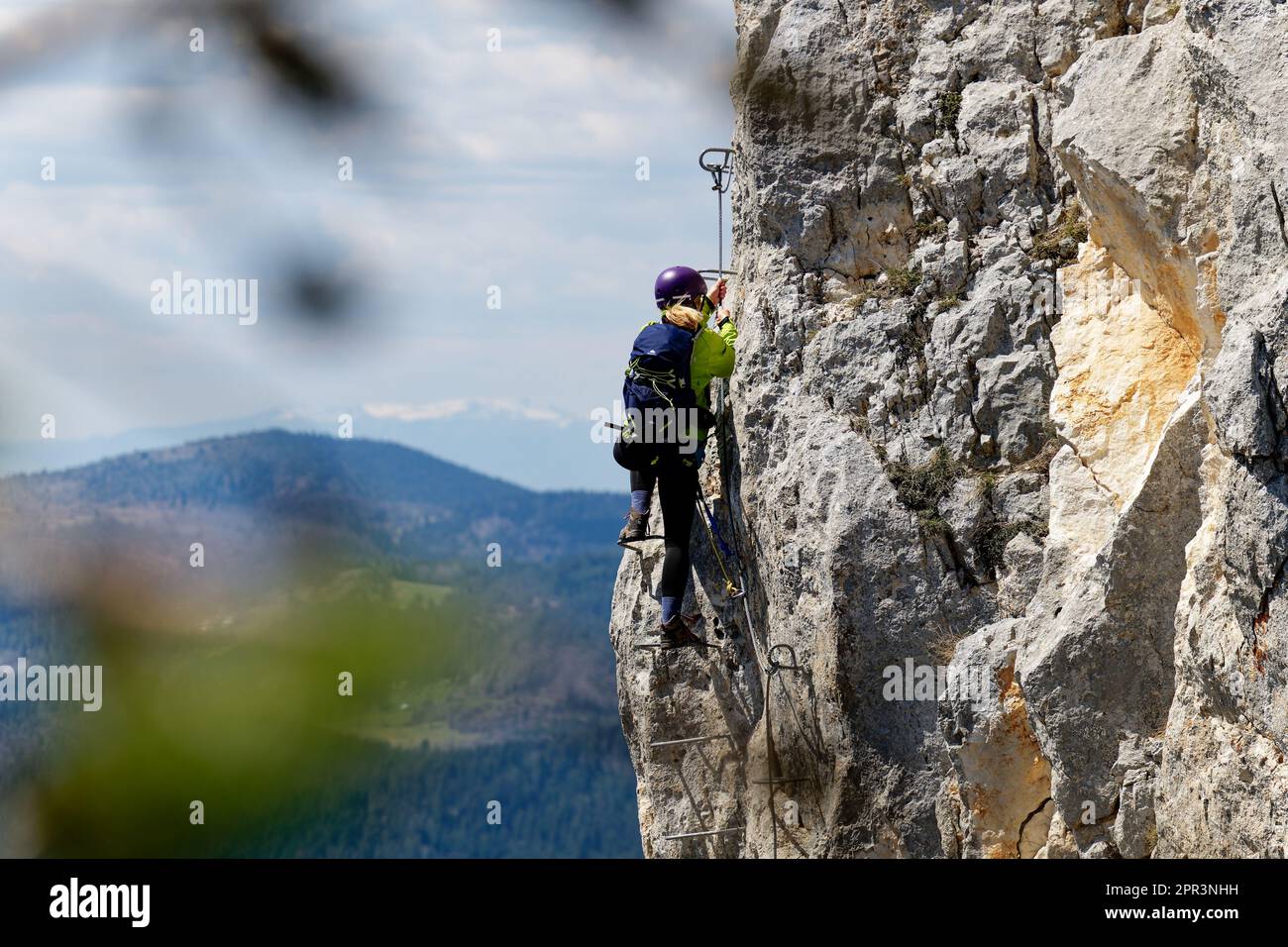 A person climbing a via ferrata route on a vertical rock wall. Sports