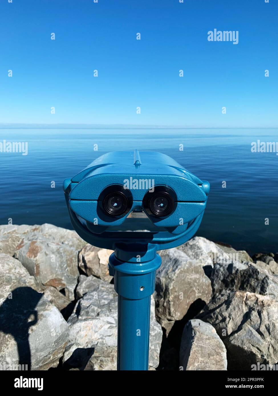 Calm Shell Telscope A blue telescope on a rocky shoreline beside a calm blue body of water ...