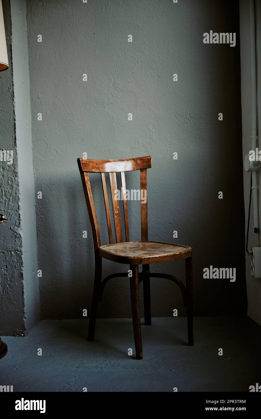 The wooden chair with intricate details adds a touch of charm to the room, while the gray wall and natural light from the window create a serene ambia Stock Photo