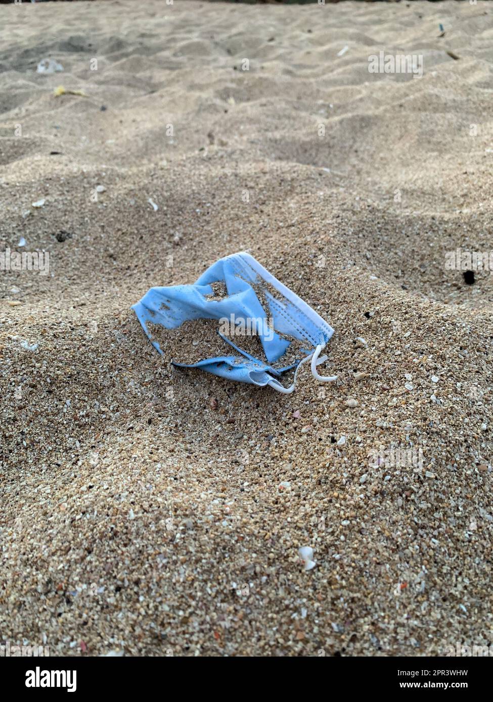 Disposable medical facemask are on a beach, covered with sand, leading