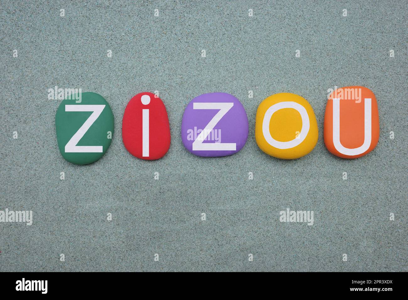 Zizou, masculine given name composed with multi colored stone letters over green sand Stock Photo