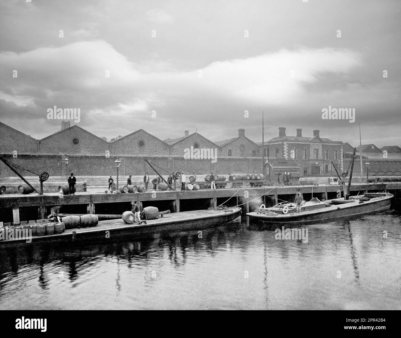 An late 19th century view of workmen loading Guinness Barrels onto barges moored to the quays on the River Liffey, Dublin, Ireland. When St. James's Gate land was leased to Arthur Guinness at £45 per year for 9,000 years, the brewery founded in 1759 has been the home of Guinness ever since. It became the largest brewery in Ireland in 1838, and the largest in the world by 1886, with an annual output of 1.2 million barrels. Stock Photo