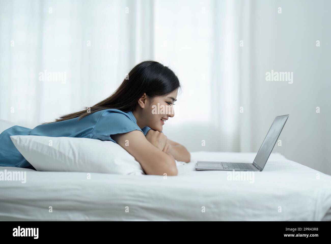 Beautiful Asian woman lying in bed and using laptop to play social ...