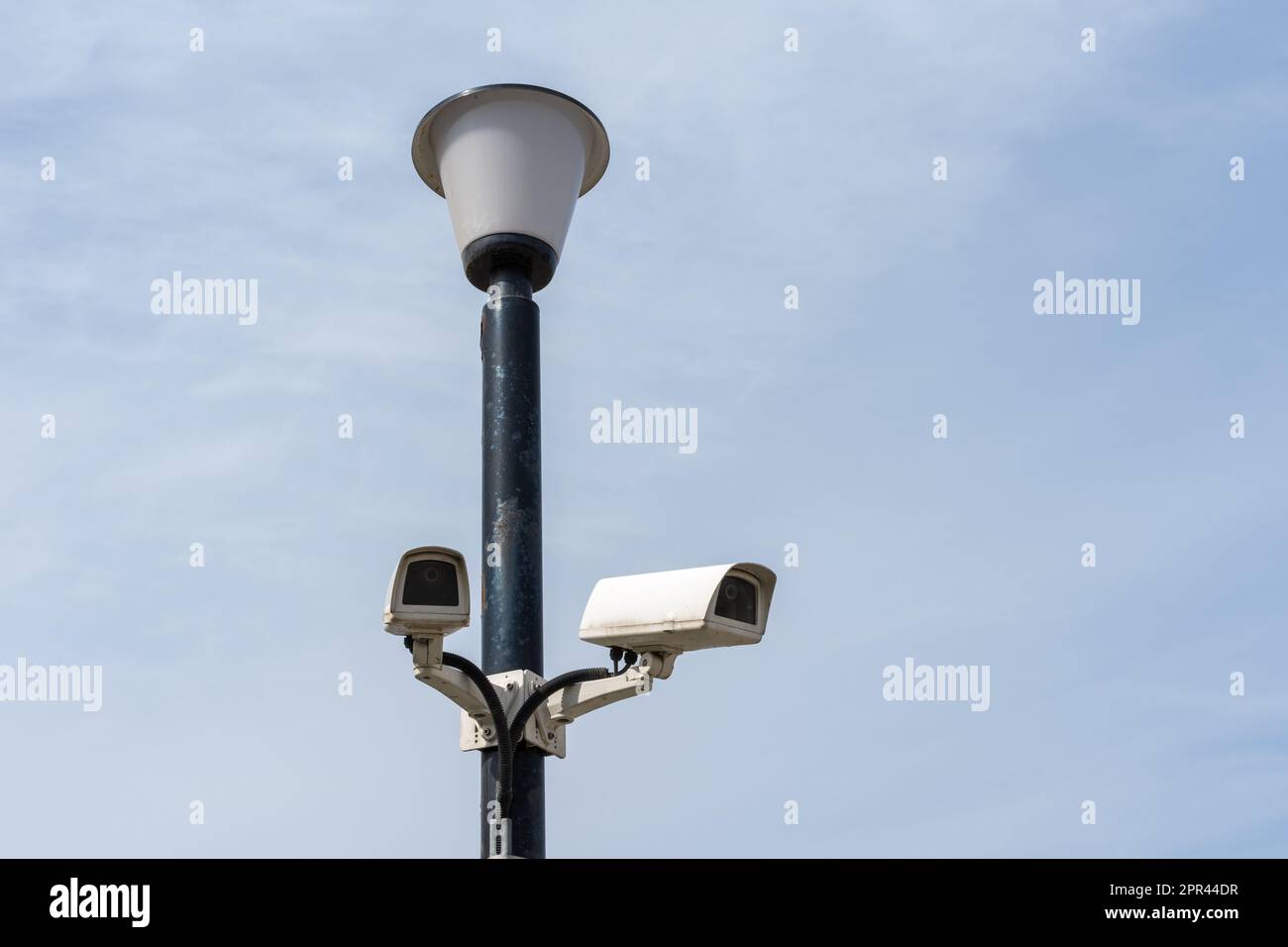 Surveillance cameras mounted on a lamp post against a blue sky