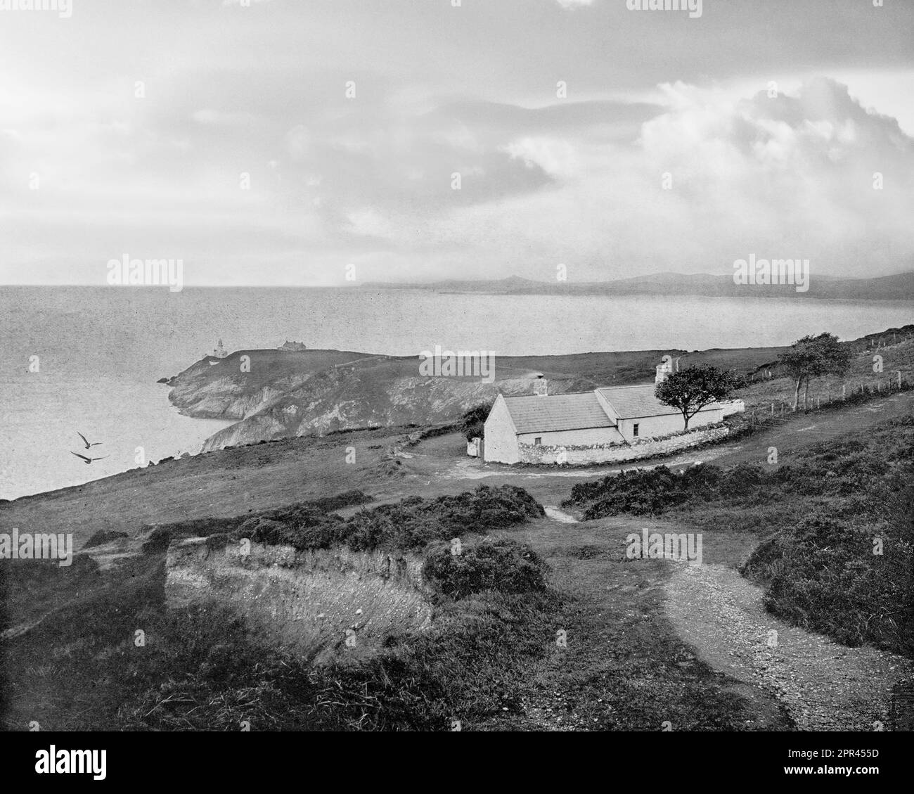 A late 19th century view of Dublin Bay from Howth Head with cottages and a distant Baily Lighthouse  A new tower, 41 metres (134 ft) above the sea, designed by George Halpin Senior, the corporation's Inspector of Works, was completed on 17 March 1814. Stock Photo