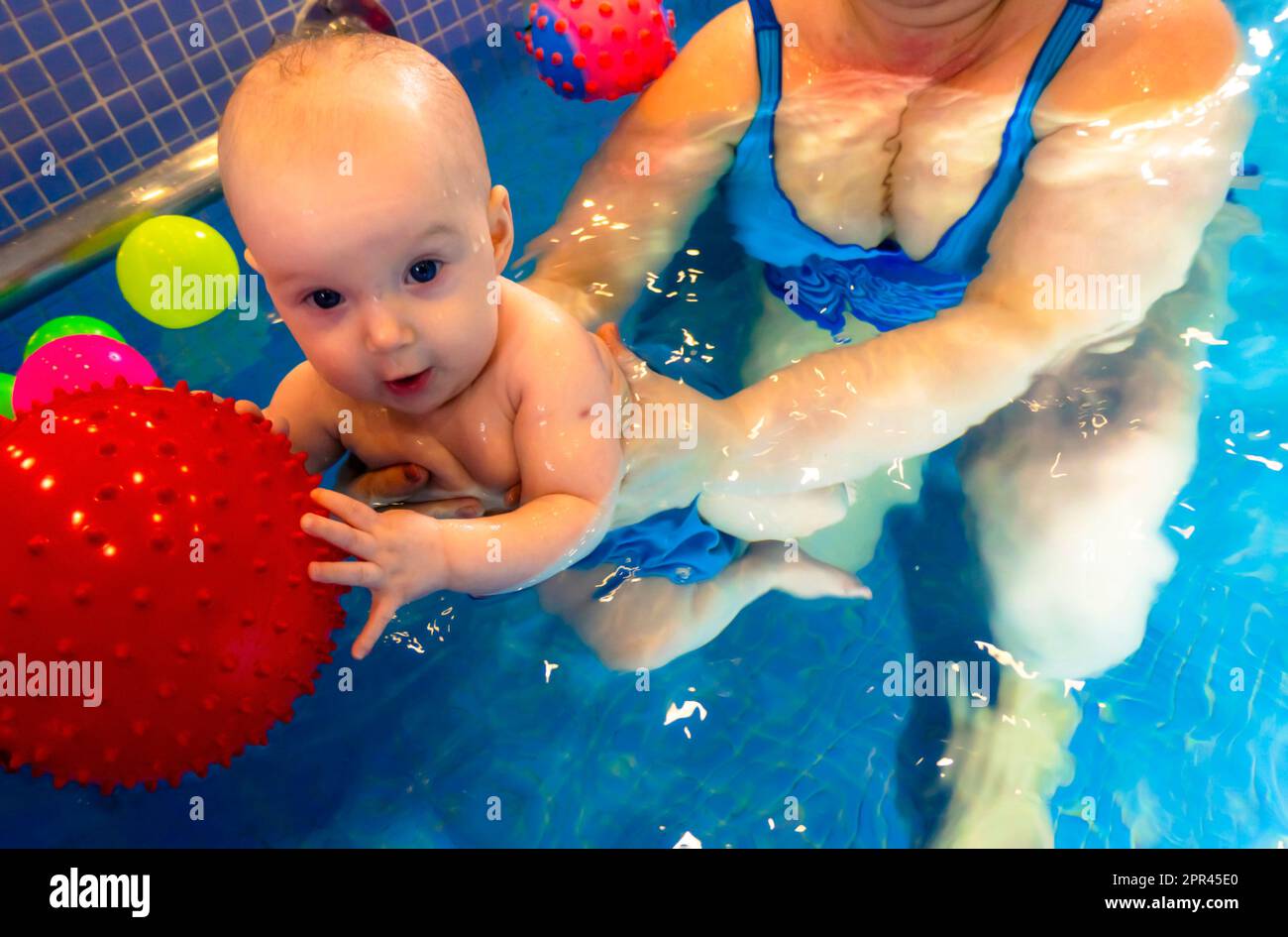Adorable baby girl enjoying swimming in a pool with her mother early development class for