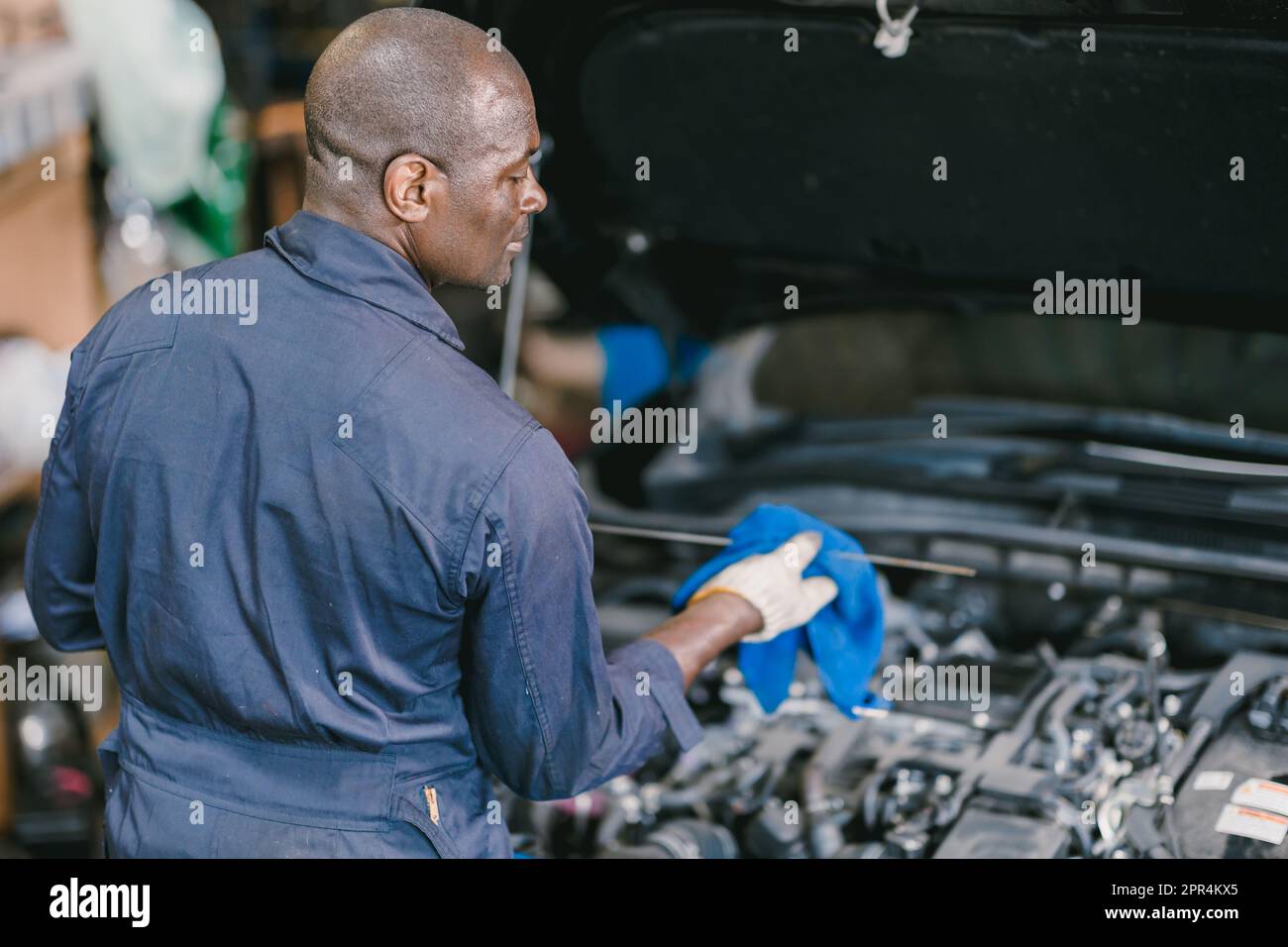 Garage Mechanic African Black male professional working car auto service checking engine oil Stock Photo