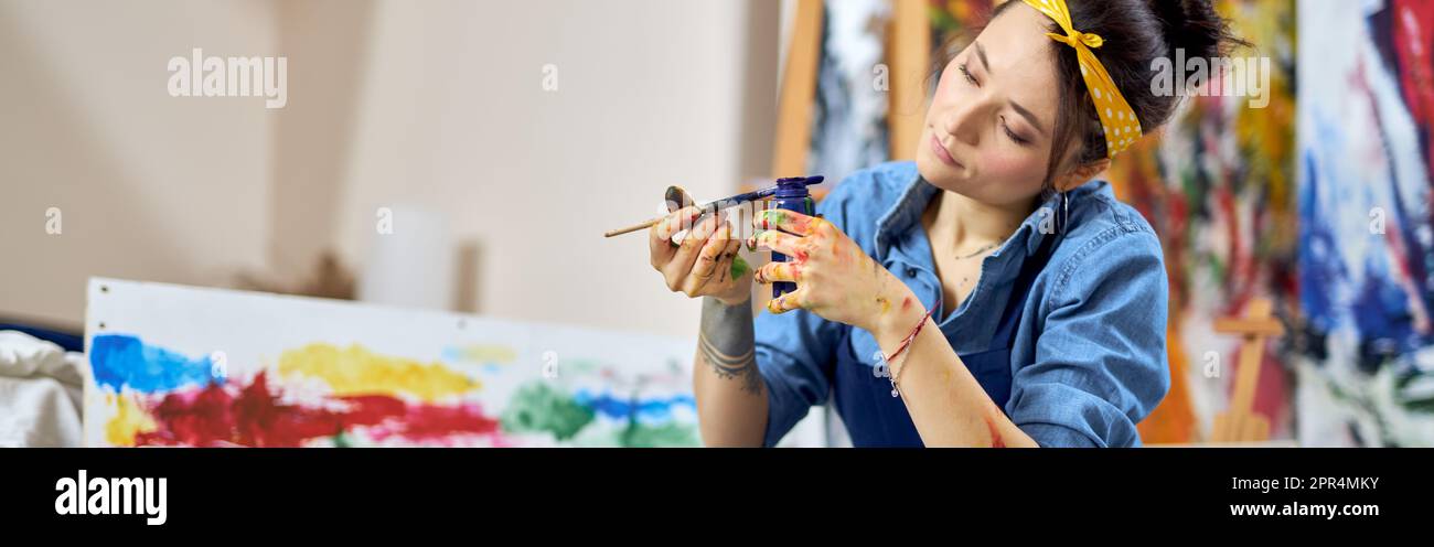 Relaxed young woman, female painter in apron holding blue paint jar and ...