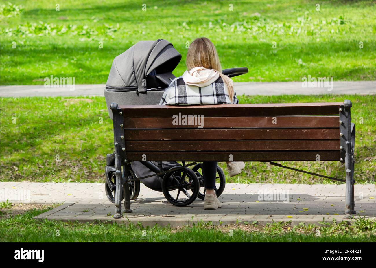 Young adult happy woman sits on a wooden bench in a city park on a warm sunny spring day. Stock Photo