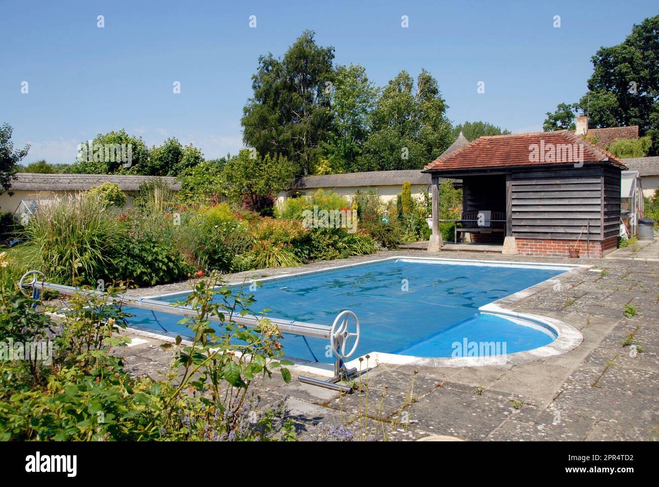 Open air swimming pool in garden, with cover in place and roller at one end to accommodate cover when not over pool Stock Photo