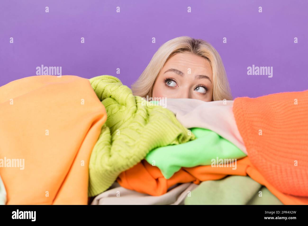 Portrait of minded person hide face behind pile stack clothes look ...