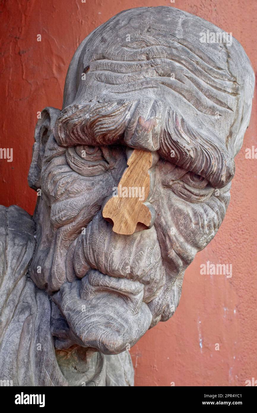 The wooden figure of a pained looking, deeply furrowed man outside an art shop in Little India, Singapore, with his nose cleanly cut off Stock Photo