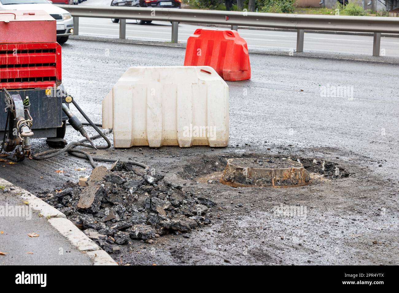 A pneumatic road compressor with a jackhammer stands near a sewer manhole being repaired on the carriageway of a city road. Copy space. Stock Photo