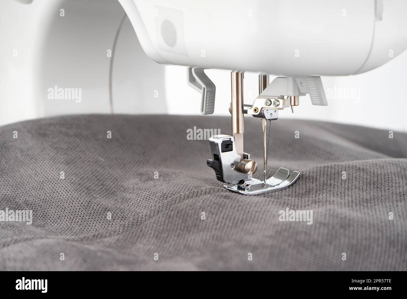 Modern sewing machine presser foot with gray fabric and thread, closeup