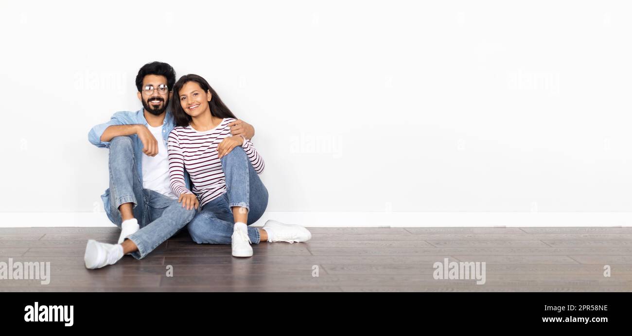 Happy indian couple sitting on floor against white wall Stock Photo - Alamy