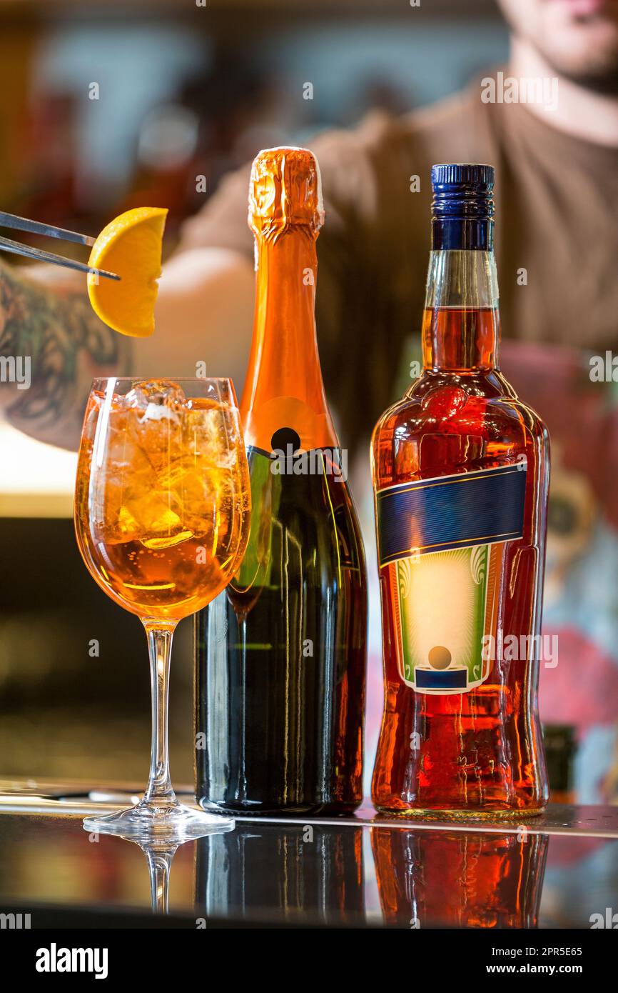 A bottle of liquor next to a glass of orange juice with ice and a