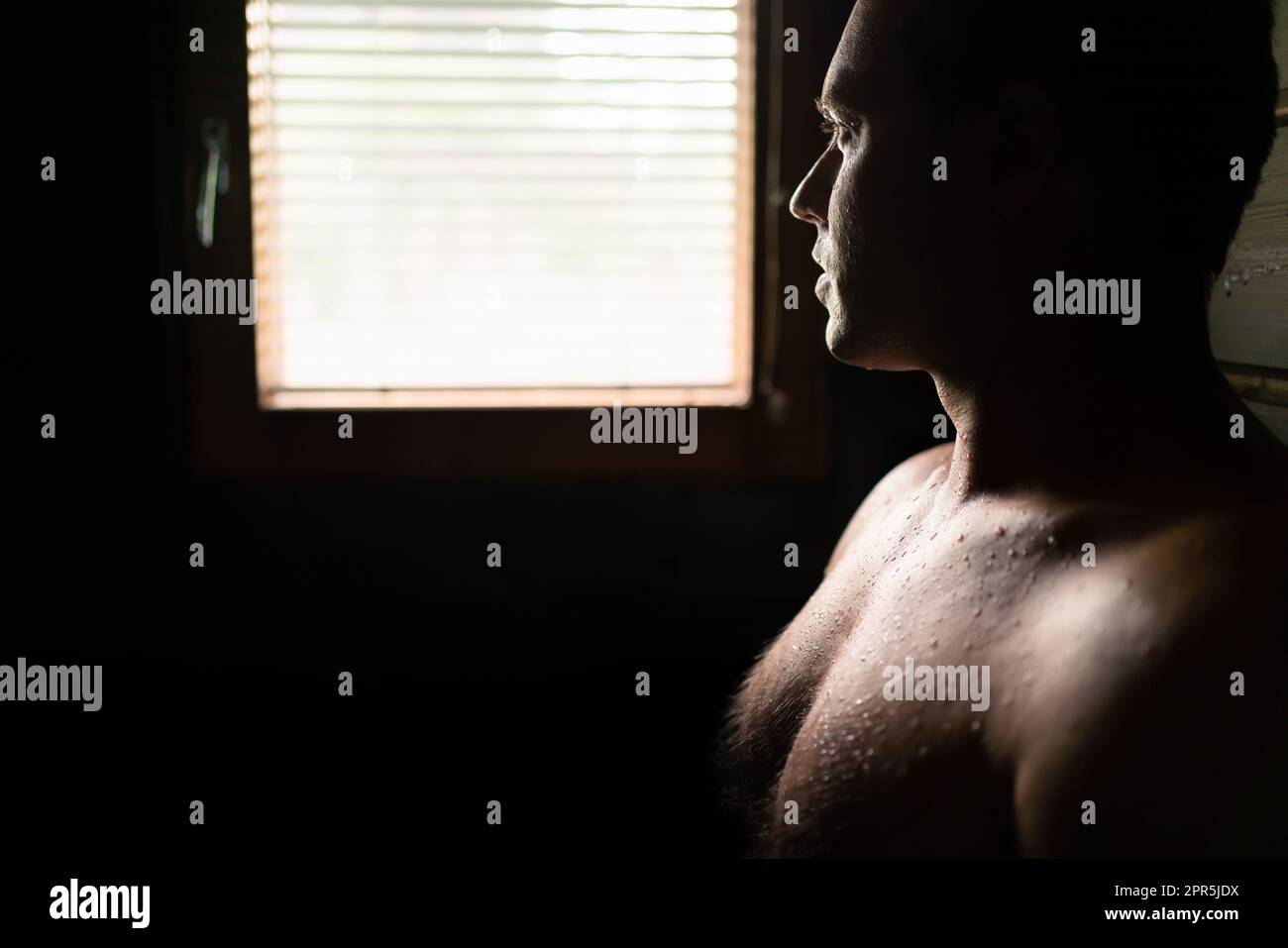 Sauna. Man in dark wood spa in Finland. Finnish wooden steam room in summer cabin. Person with sweat on skin and body.  Traditional wellness. Stock Photo