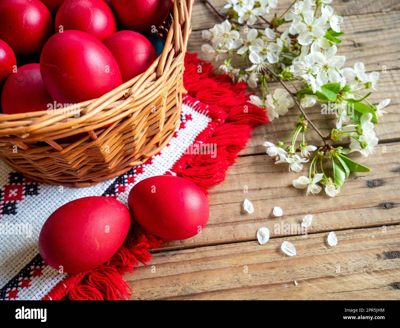 basket of red Easter eggs next to flowering branches on wooden table Stock Photo